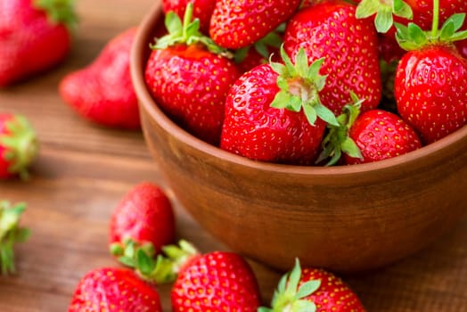 Fresh juicy organic strawberries in a clay bowl. Ripe red strawberries in a bowl on a wooden background.