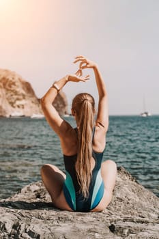 Yoga on the beach. A happy woman meditating in a yoga pose on the beach, surrounded by the ocean and rock mountains, promoting a healthy lifestyle outdoors in nature, and inspiring fitness concept