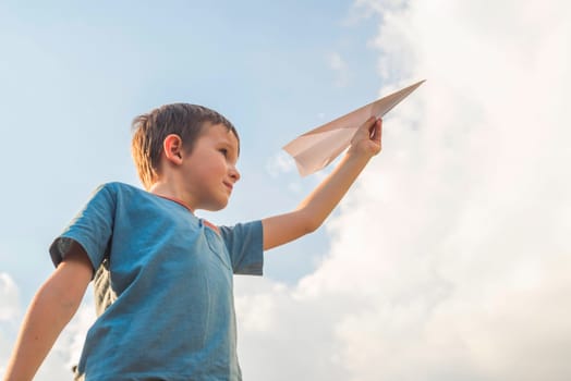 Happy child playing with paper airplane against the sky. A boy with paper airplane.