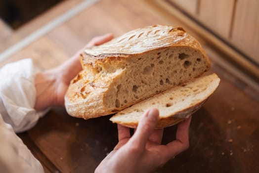 Fresh baked bread in hands of a hostess in the kitchen