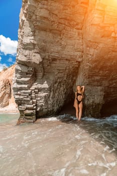Woman travel sea. Attractive blonde woman in a black swimsuit enjoying the sea air on the seashore around the rocks. Travel and vacation concept