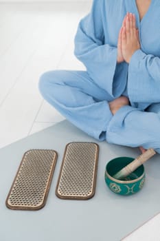 Asian woman sitting on yoga mat with tibetan singing bowl and sadhu boards