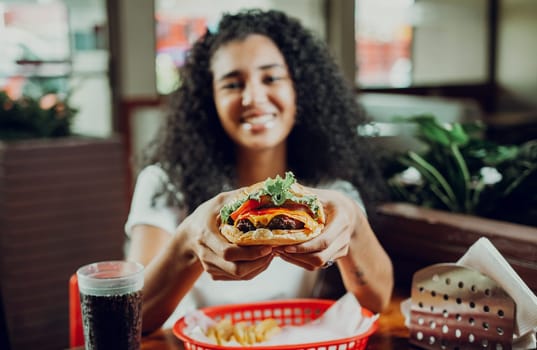 Happy girl showing burger in a restaurant. Close-up of a girl showing appetizing hamburger in a restaurant