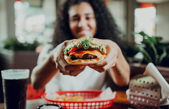 Smiling girl showing a burger in a restaurant. Close-up of a woman showing appetizing hamburger in a restaurant