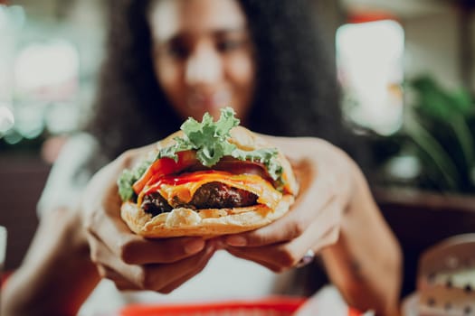 Close-up of a girl showing appetizing hamburger in a restaurant. Hands of girl showing burger in a restaurant