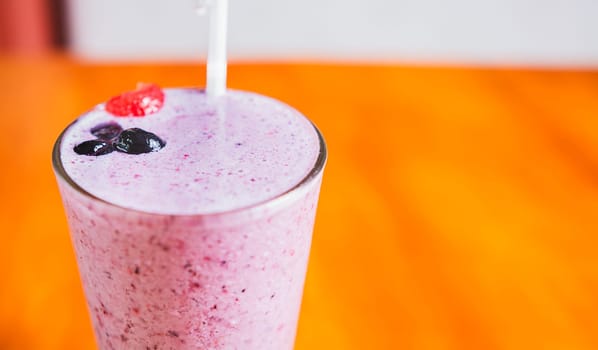 Close up of a strawberry milkshake in blurred background with copy space. Strawberry smoothie with blueberry on wooden background