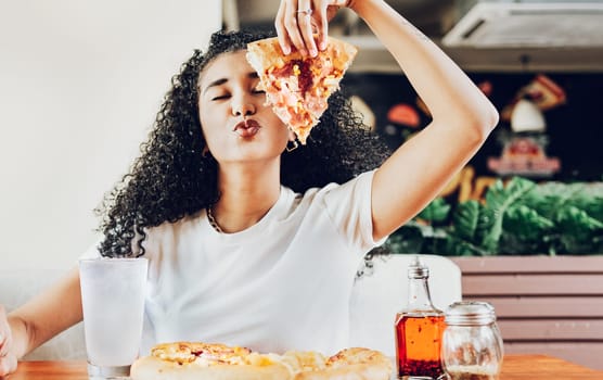 Girl in a restaurant showing slice of pizza giving a kiss to the camera. Beautiful curly haired woman showing slice of pizza in a restaurant with copy space
