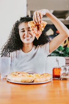 Smiling afro woman enjoying a pizza in a restaurant. Happy afro hair woman showing slice of pizza in a restaurant