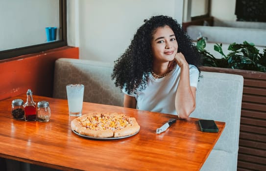 Beautiful afro hair girl in a pizzeria restaurant. Lifestyle of afro-haired girl sitting in a pizzeria