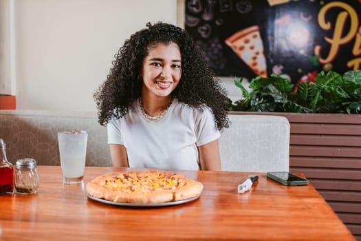 Smiling Young curly haired woman sitting in a pizzeria. Portrait of a beautiful girl in a pizzeria