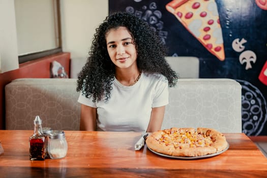 Portrait of a beautiful girl in a pizzeria. Young curly haired woman sitting in a pizzeria