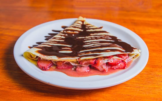 Close up of sweet strawberry crepe with chocolate cream on wooden table. Crepe with chocolate cream and strawberry on wooden table