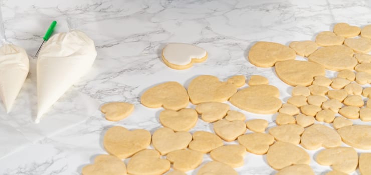 Decorating heart-shaped sugar cookies with pink and white royal icing for Valentine's Day.