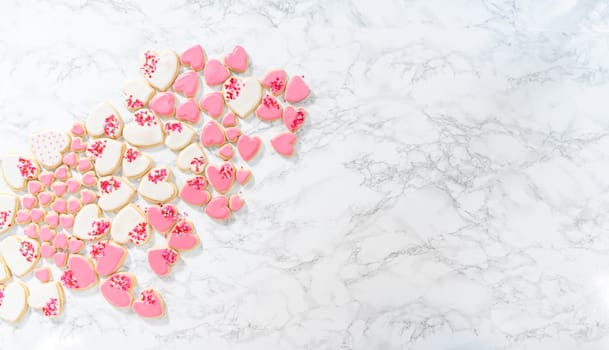 Flat lay. Decorating heart-shaped sugar cookies with pink and white royal icing for Valentine's Day.