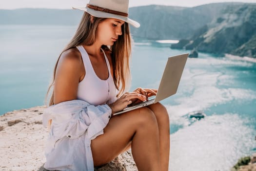 Digital nomad, Business woman working on laptop by the sea. Pretty lady typing on computer by the sea at sunset, makes a business transaction online from a distance. Freelance remote work on vacation