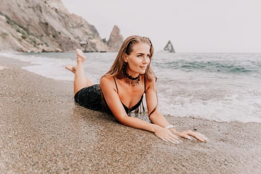 Woman travel sea. Young Happy woman in a long red dress posing on a beach near the sea on background of volcanic rocks, like in Iceland, sharing travel adventure journey