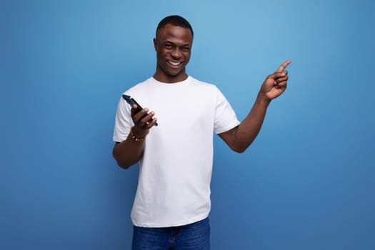 cheerful 30s african man with short haircut in white t-shirt with smartphone.