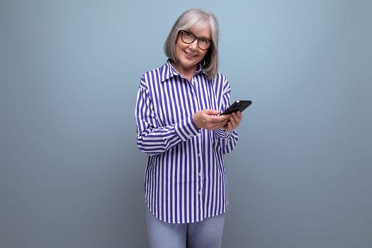 modern 50s middle aged woman with gray hair in trendy outfit mastering smartphone on bright studio background with copyspace.