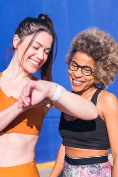 vertical portrait of two multiethnic friends using a smart watch while practicing sport, concept of sports technology and active lifestyle, copy space for text
