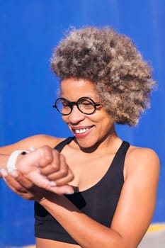 vertical photo of a sporty african american woman using smart watch outdoors in a sunny day, concept of sports technology and active lifestyle