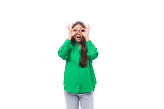 well-groomed slender brunette woman with long hair dressed in a casual green shirt makes faces.
