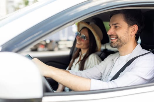 Smiling positive couple husband and wife going summer vacation by car white together. Happy millennial man and woman wearing wicker hat and sunglasses sitting in auto, enjoying road trip