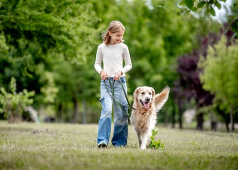 Preteen girl with golden retriever dog walking at nature. Cute child kid with purebred pet doggy labrador in park at summer