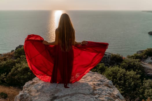 Woman sunset sea red dress, side view a happy beautiful sensual woman in a red long dress posing on a rock high above the sea on sunset