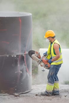 A worker cuts concrete with a special saw. The process of cutting a hole in a concrete ring designed to be buried underground. Dust scatters in different directions during the sawing process