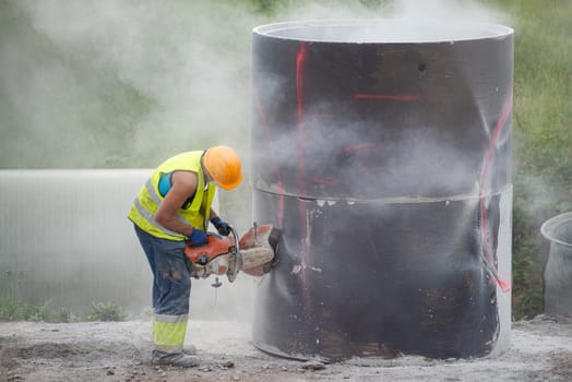 Reconstruction of the road in the city. A worker cuts holes in a concrete barrel to collect rainwater installed under the pavement. Use of a helmet and respirator, compliance with safety regulations