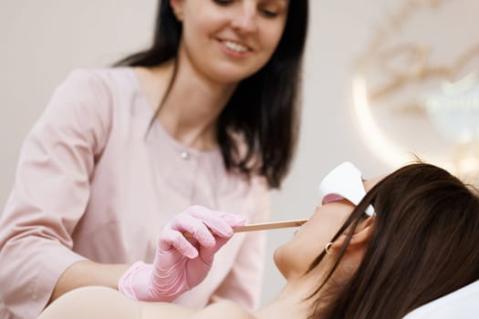 Hair removal depilation. Sugar bodycare. Sugaring bodycare cosmetics. Laser hair removal. Beautician holds a wooden spatula and applies a transparent gel with anesthetic to the woman's face