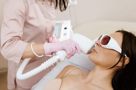 Therapist beautician makes a laser treatment to young woman's face at beauty SPA clinic. Facial laser hair removal epilation procedures. Skin care, cosmetic procedures.