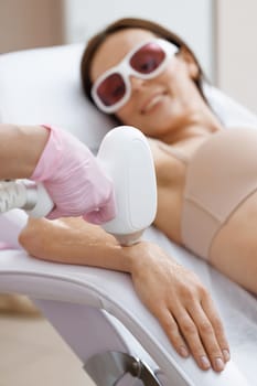 Young woman getting laser hair removal treatment on wrist, close-up. Dermatology, photorejuvenation. Cosmetic clinic. Laser epilation. Hair removal depilation. Sugar bodycare.