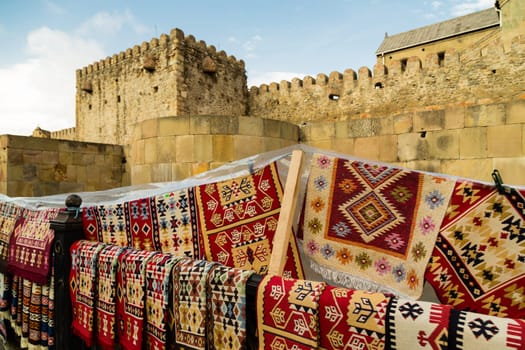 Europe, Georgia - stone yellow wall of an ancient temple, handmade carpets with beautiful ornaments for sale. High quality photo