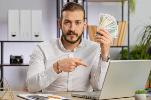 Young middle eastern boss business man showing money dollar cash gives to you wages salary, satisfied with good work. Success, wealth, investment. Freelancer guy at office workplace looking at camera