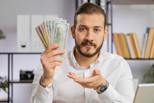 Young middle eastern boss business man showing money dollar cash gives to you wages salary, satisfied with good work. Success, wealth, investment. Freelancer guy at office workplace looking at camera
