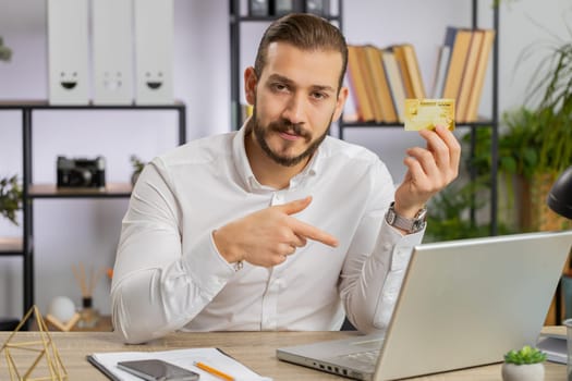 Business man showing plastic credit bank card advertising transferring money cashless on laptop computer, purchases online shopping, sale discount, internet order purchase. Guy at office workplace