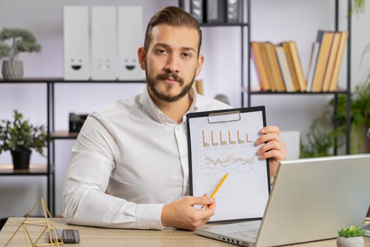 Young middle eastern boss business man making online presentation video call, demonstrates graphic analytics, planning budget, statistic. Freelancer guy at office workplace looking at camera, talking