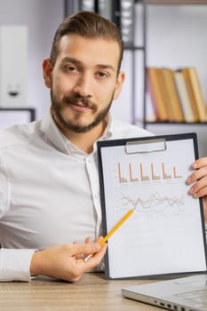 Young boss business man making online presentation video call, demonstrates graphic analytics, planning budget, statistic. Freelancer guy at office workplace looking at camera, talking. Vertical shot