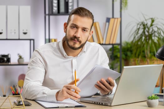Businessman ceo reading business contract, planning project, analyzing resume, satisfied with good paperwork results. Man at office workplace looking at camera talking, online conversation interview