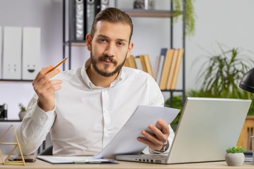 Businessman ceo reading business contract, planning project, analyzing resume, satisfied with good paperwork results. Man at office workplace looking at camera talking, online conversation interview