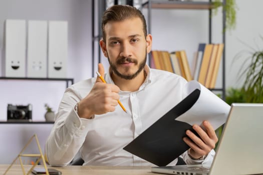 Businessman ceo reading business contract, planning project, analyzing resume, satisfied with good paperwork results. Man at office workplace looking at camera talking, online conversation interview