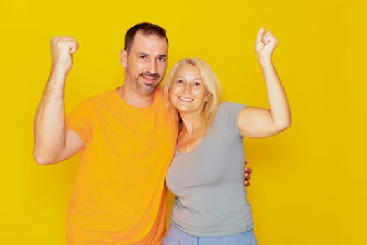 Real caucasian couple in their 40s with raised fists celebrating successful action isolated over yellow background