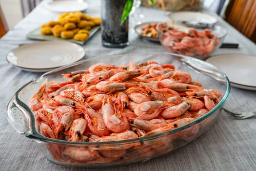 A dish of unpeeled shrimp on a dinner table with plates. Seafood diner. Boiled shrimps. vegetarian dinner, food.