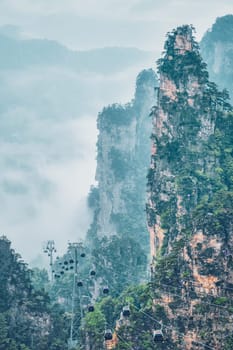 Famous tourist attraction of China - Zhangjiajie stone pillars cliff mountains in fog clouds with cable railway car lift at Wulingyuan, Hunan, China. With camera pan