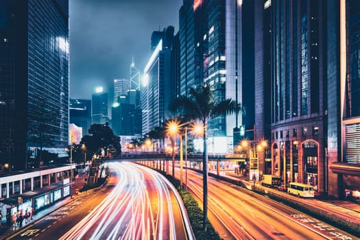 Street traffic in Hong Kong at night. Office skyscraper buildings and busy traffic on highway road with blurred cars light trails. Hong Kong, China