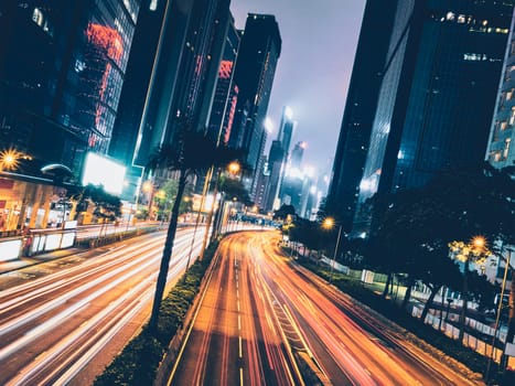 Street traffic in Hong Kong at night. Office skyscraper buildings and busy traffic on highway road with blurred cars light trails. Hong Kong, China