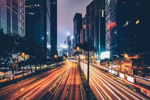 Street traffic in Hong Kong at night. Office skyscraper buildings and busy traffic on highway road with blurred cars light trails. Hong Kong, China