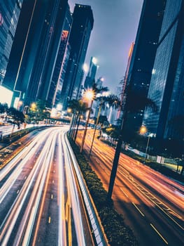 Street traffic in Hong Kong at night. Office skyscraper buildings and busy traffic on highway road with blurred cars light trails. Hong Kong, China