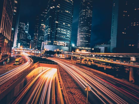 Street traffic in Hong Kong at night. Office skyscraper buildings and busy traffic on highway road with blurred cars light trails. Hong Kong, China